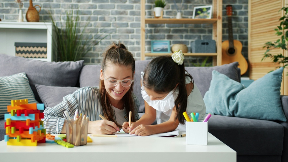 An adult and a child drawing together at a low table, coloured building blocks beside them